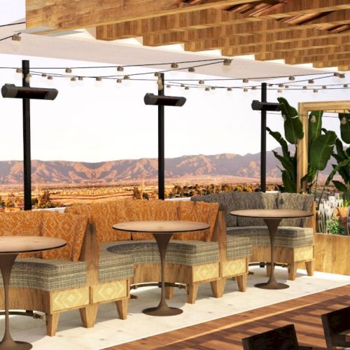 An open-air, rooftop lounge with cushioned seating, wooden accents, hanging lights, and panoramic mountain views, decorated with plants.