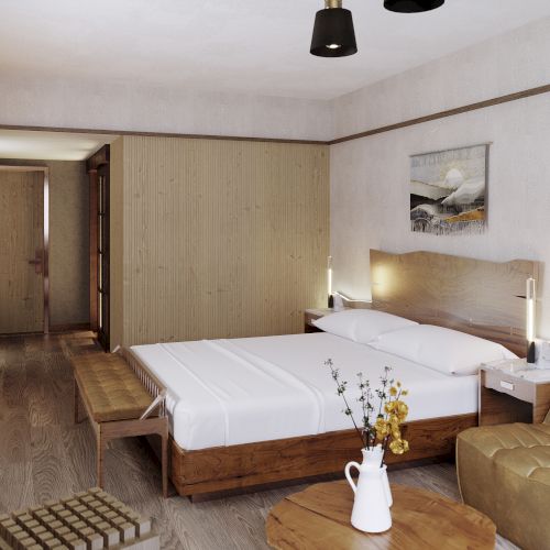 This image shows a modern hotel room with a double bed, sofa, coffee table, and decor items. It has wooden floors and neutral tones.