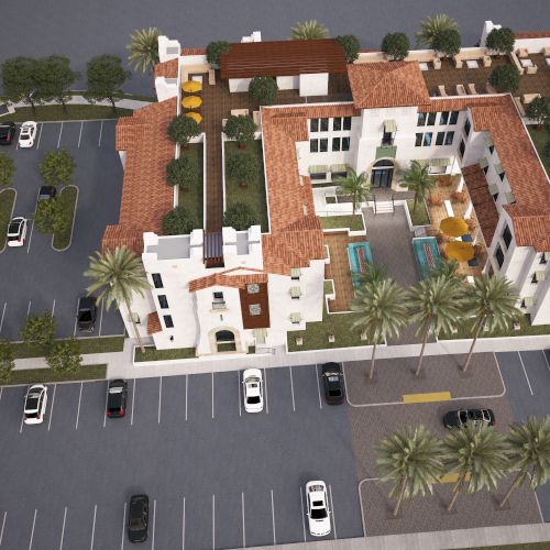 This image shows an aerial view of a Mediterranean-style building with a red-tile roof, parking lots, green spaces, and palm trees surrounding it.